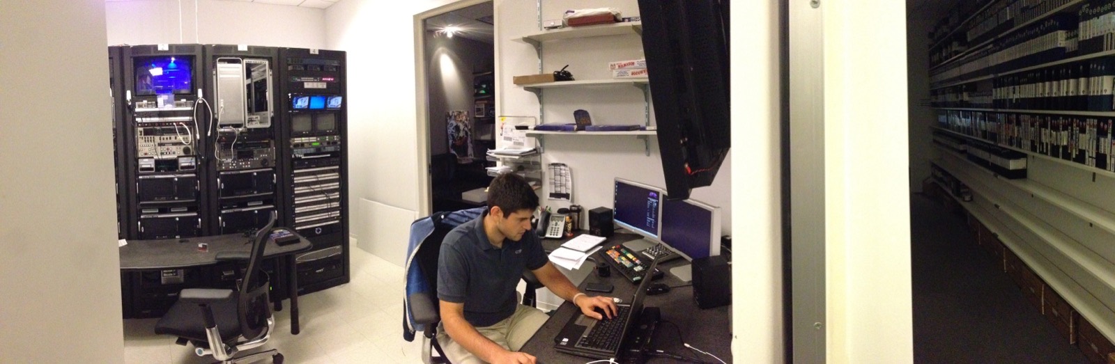 An edit suite lined with equipment racks and a wall of tape stock, Justin working at the keyboard.