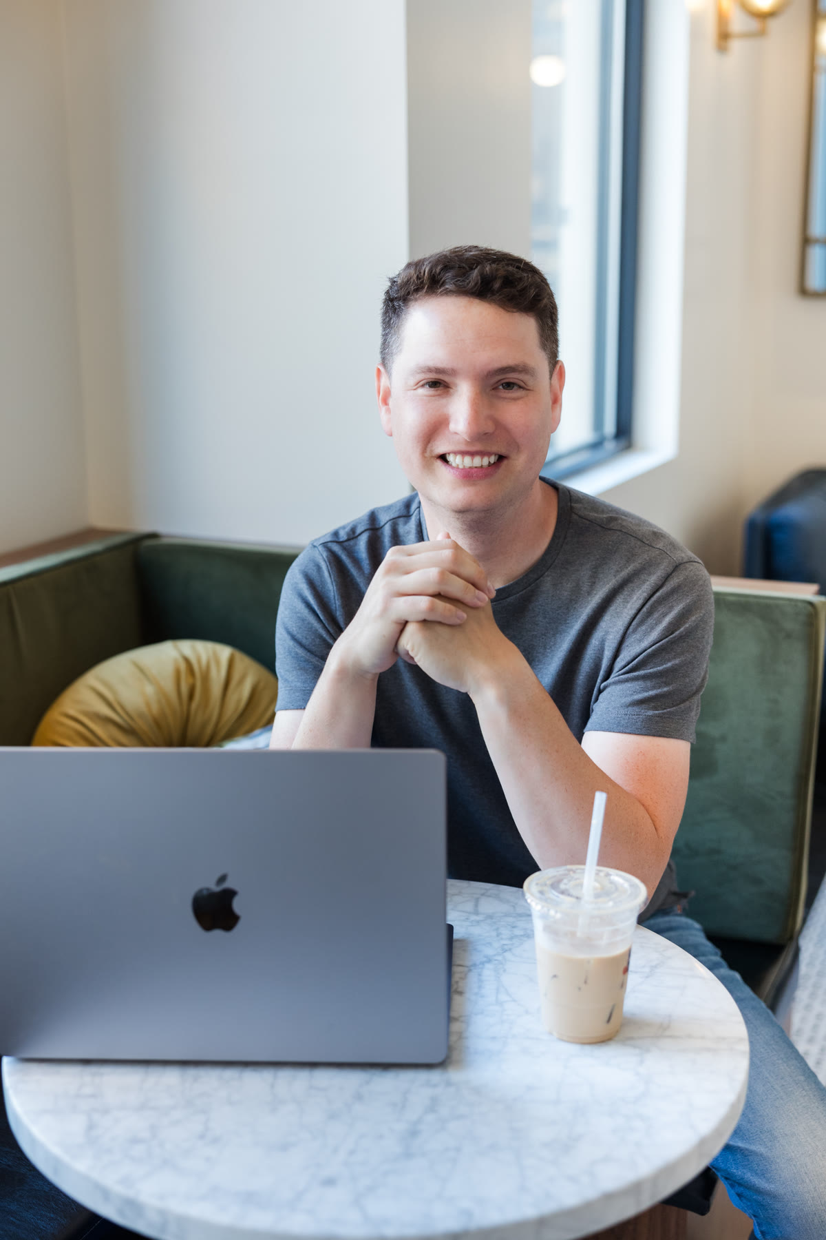 Justin Herrera at a caf&eacute; table, laptop open, iced coffee in reach