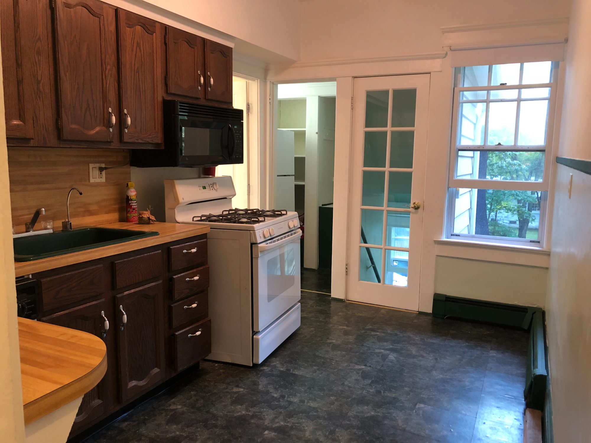 The kitchen as bought: dark oak cabinets, butcher block, a green sink and a French door to the landing.