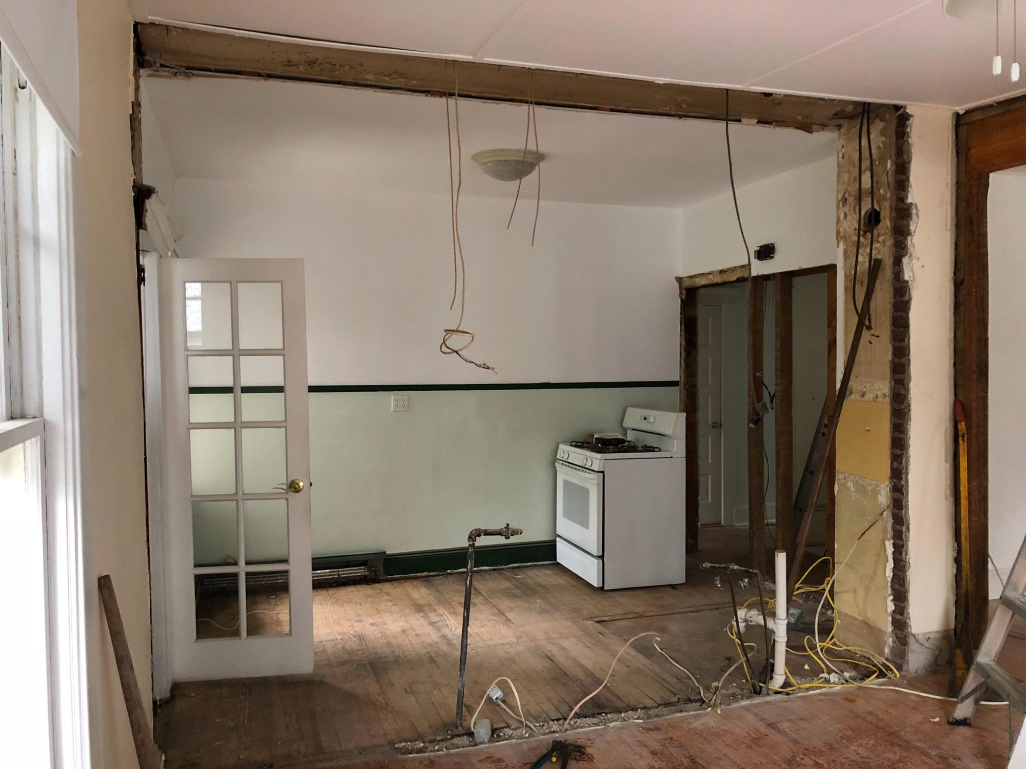 The main floor mid-demolition: the load-bearing wall opened up to a raw beam, plaster off, the old stove still standing.