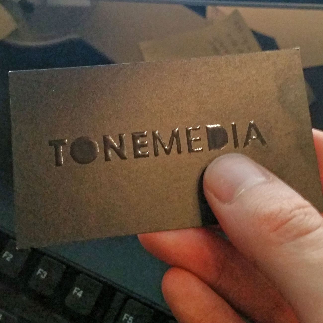 A hand holding an embossed Tonemedia business card.