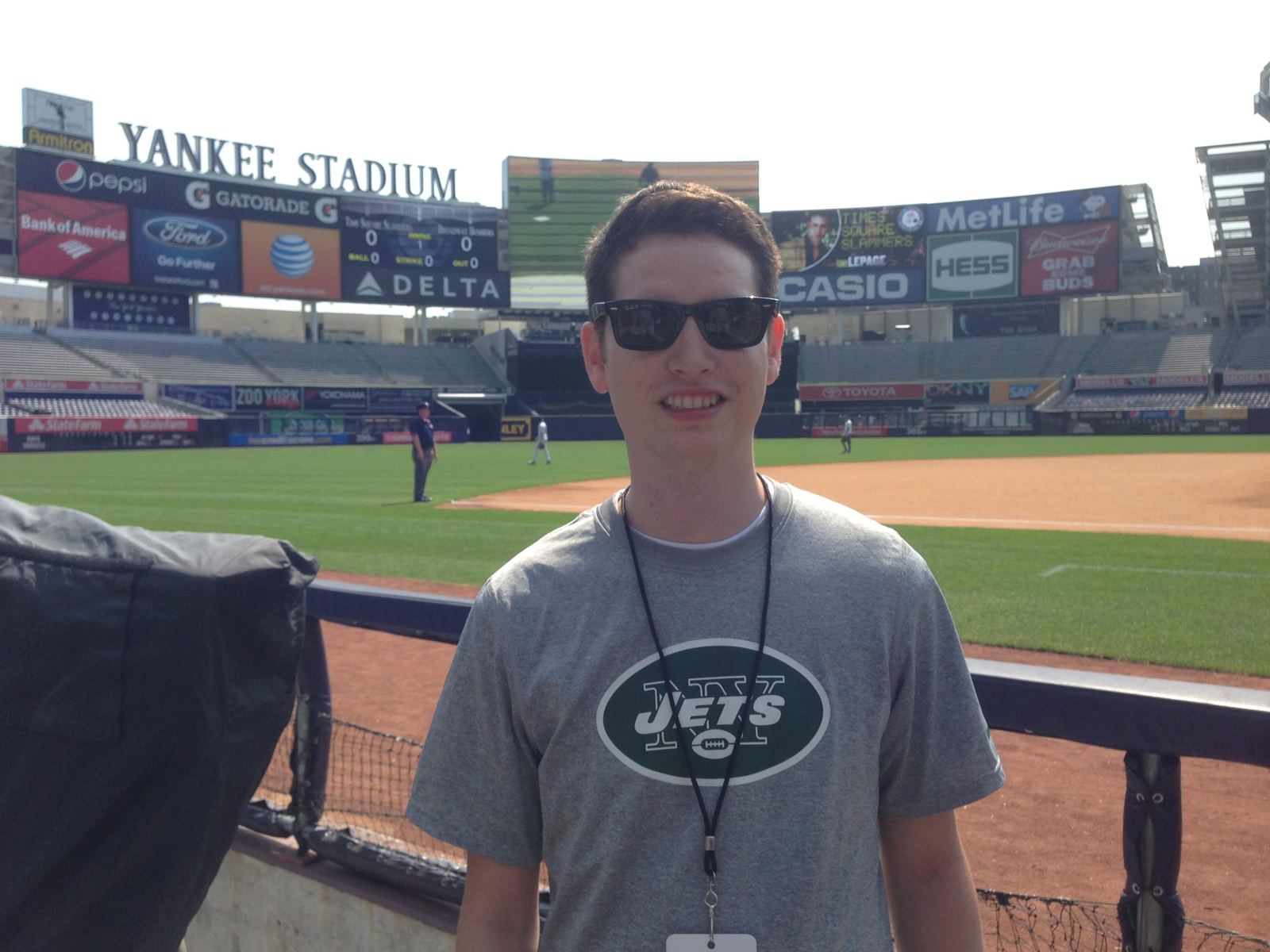 A young Justin Herrera in a Jets t-shirt and credential lanyard, standing in front of the field at Yankee Stadium.