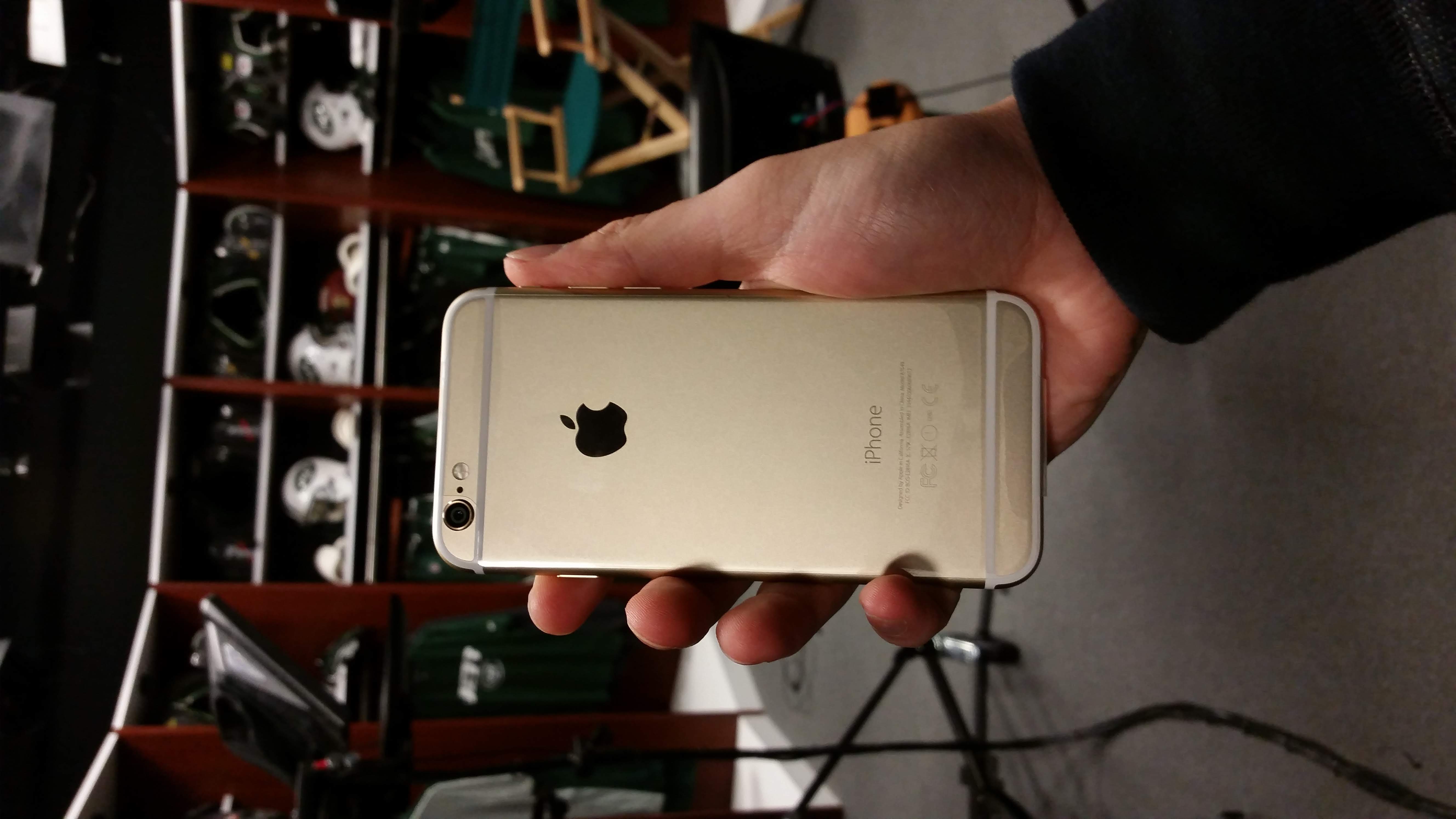 A gold iPhone 6 held up in front of New York Jets helmets in the team offices, 2014.